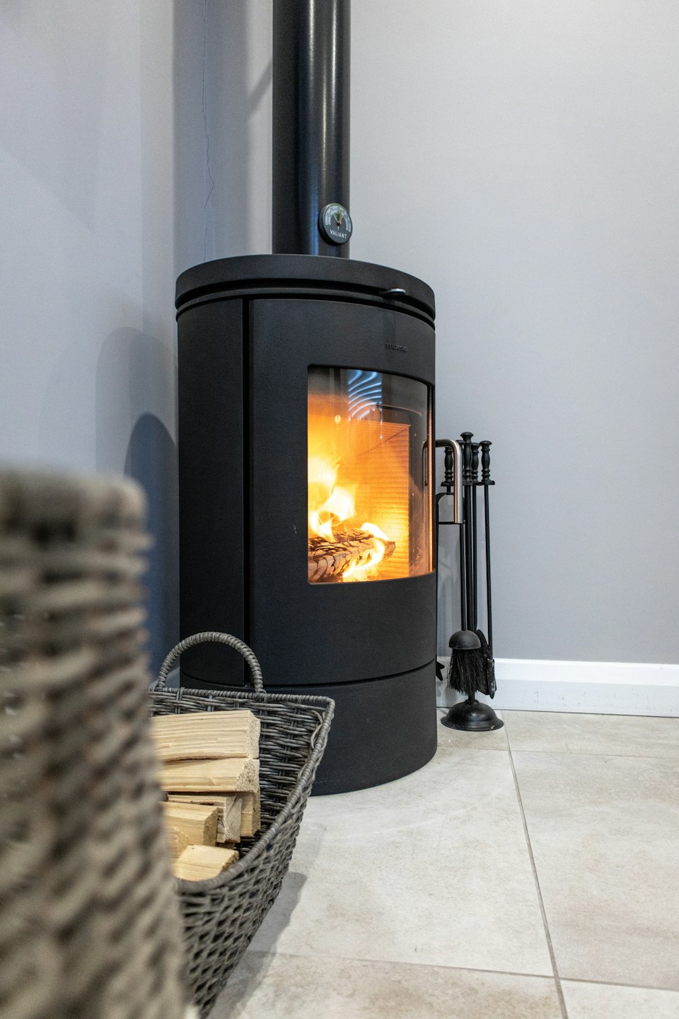 Burning wood stove with glass door and basket of firewood.