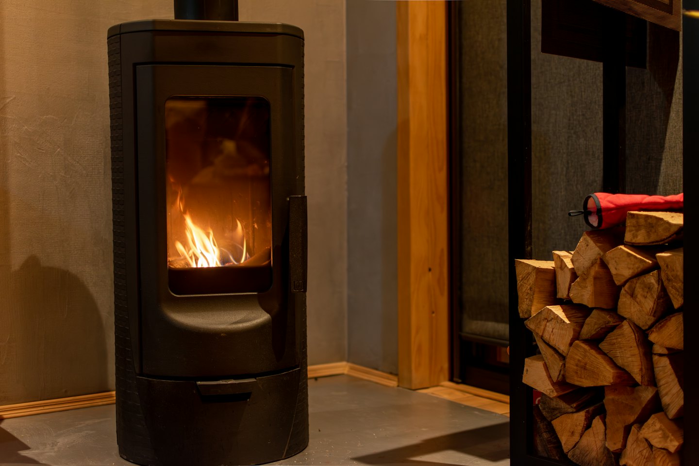 Black wood burning stove with burning flames next to stacked firewood.